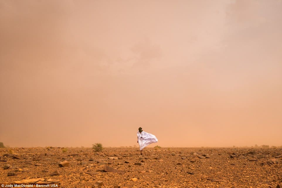A Mauritanian man walking through a sand storm in the Sahara desert.
